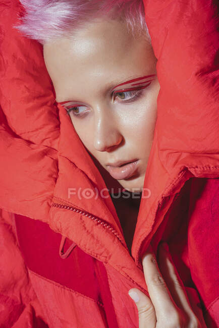 Портрет молодої жінки з коротким рожевим волоссям у червоній куртці перед червоним фоном. — стокове фото