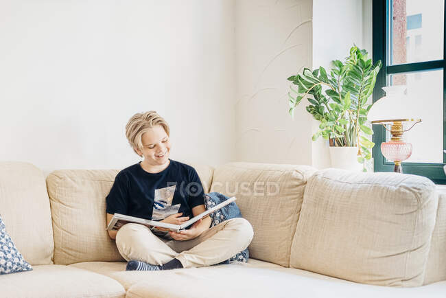 Счастливый мальчик сидит на диване в гостиной дома и читает книгу — стоковое фото