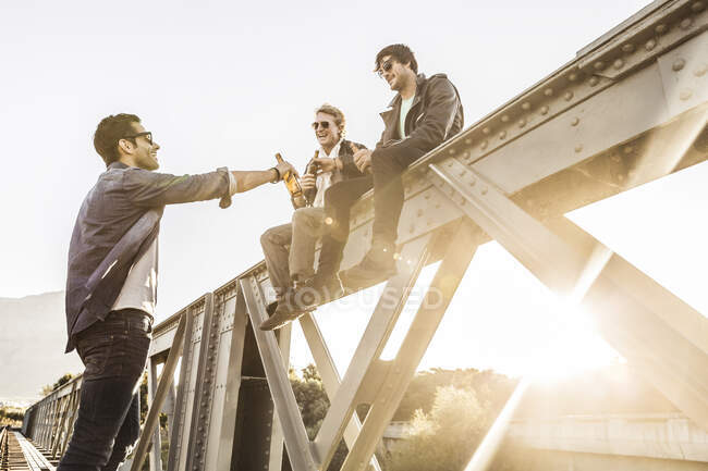 Three men drinking beer on an old railway bridge — Stock Photo