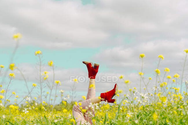 Pernas de uma mulher usando botas vermelhas no tornozelo deitado em um prado de flores na primavera — Fotografia de Stock