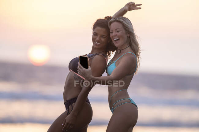 Dos mujeres felices tomando selfie en la playa al atardecer, Costa Rica - foto de stock
