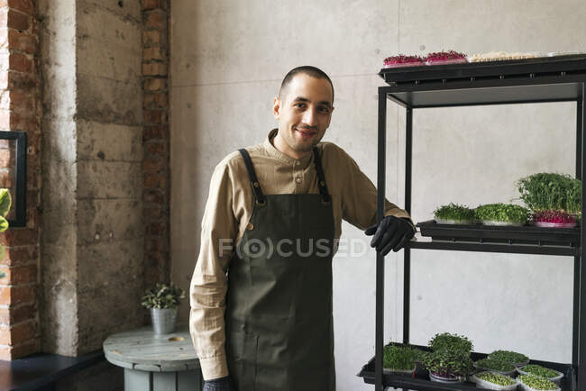 Портрет улыбающегося мужчины, стоящего на полке с микрозеленью — стоковое фото