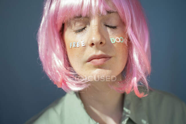 Young woman wearing pink wig, letters on her face, free doom, with eyes closed — Stock Photo