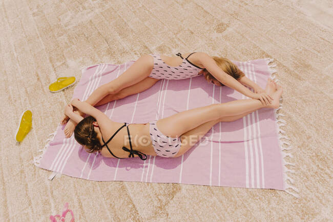 Two girls in swimsuits lying on blanket building circle — Stock Photo