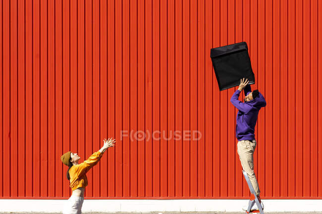 Giovane uomo e donna che si esibiscono con una scatola davanti a un muro rosso — Foto stock