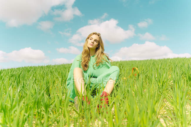 Retrato de una joven rubia vestida de verde sentada en un campo - foto de stock