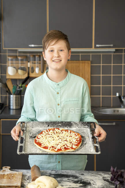 Portrait of smiling boy holding baking tray with raw homemade pizza — Stock Photo