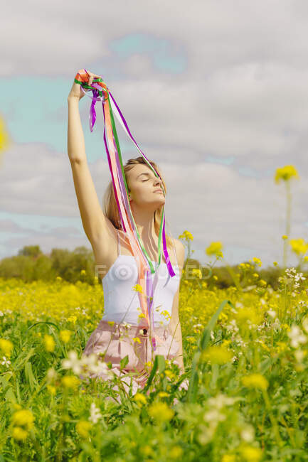 Young woman with colourful ribbons in a flower meadow in spring — Stock Photo