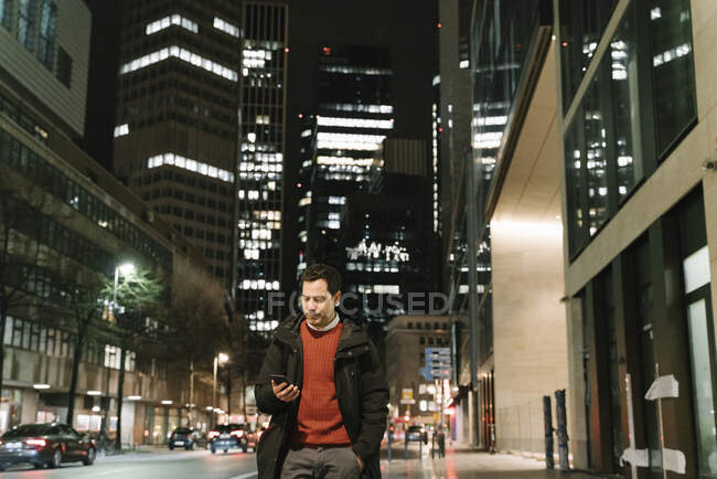 Empresário na cidade à noite olhando para smartphone, Frankfurt, Alemanha — Fotografia de Stock