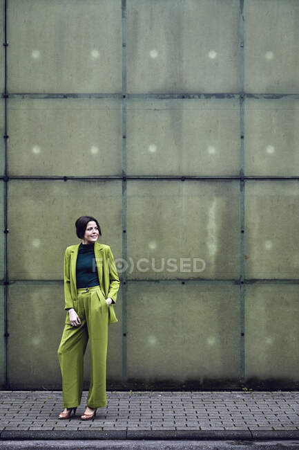Elegant businesswoman wearing green suit standing at a wall — Stock Photo