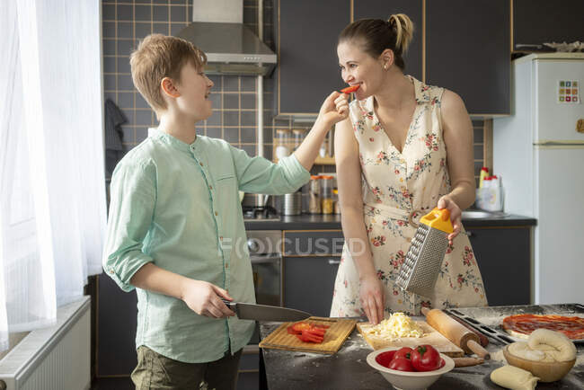 Boy feeding his mother with tomato slice in the kitchen — Stock Photo