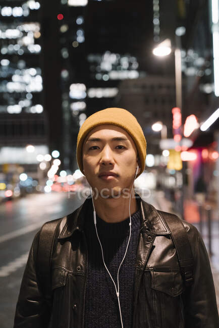Portrait of stylish man with yellow hat and earphones in the city at night — Stock Photo