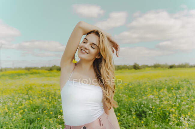 Улыбающаяся молодая женщина, стоящая на цветочном лугу весной с цветком во рту — стоковое фото