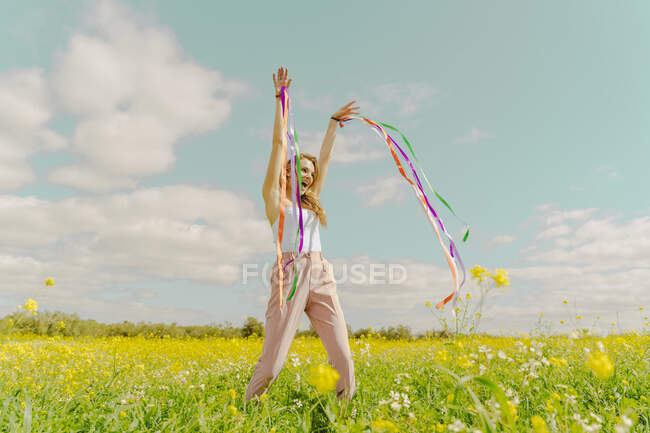 Mujer joven feliz moviéndose con cintas de colores en un prado de flores en primavera - foto de stock