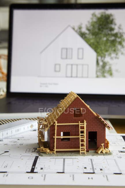 Архитектурная модель владения домом по плану строительства, ноутбук на заднем плане — стоковое фото