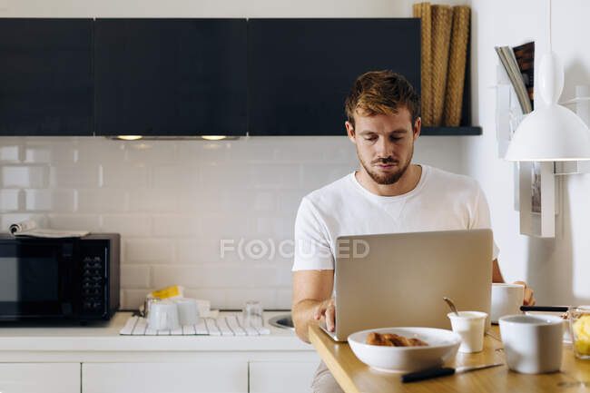 Young man using laptop in kitchen — Stock Photo