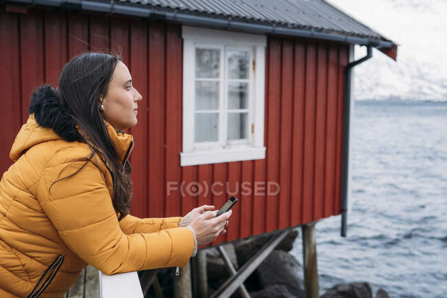 Touriste avec téléphone portable dans une cabane sur la côte, Lofoten, Norvège — Photo de stock