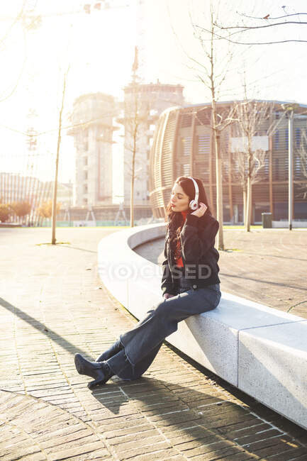 Hermosa mujer sentada en un banco y usando un teléfono inteligente, escuchando música - foto de stock