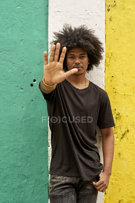Retrato de jovem com afro em pé na frente da mão levantando parede colorida — Fotografia de Stock