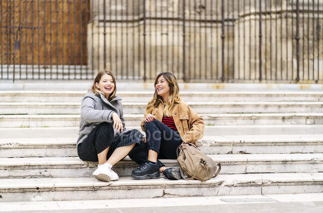 Dos jóvenes felices sentadas en las escaleras de la ciudad - foto de stock