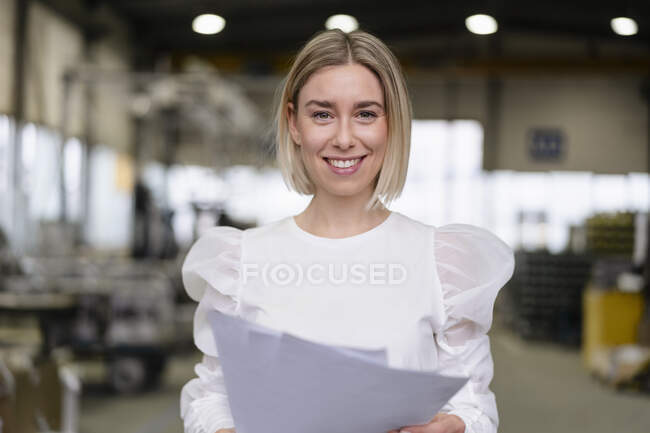 Portrait d'une jeune femme souriante tenant des papiers dans une usine — Photo de stock