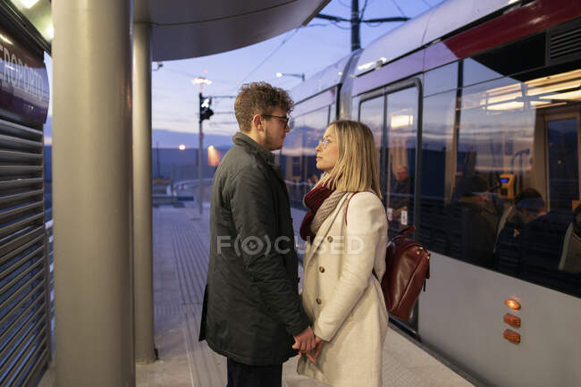 Young couple in love standing at tram stop in the evening looking at each other — Stock Photo