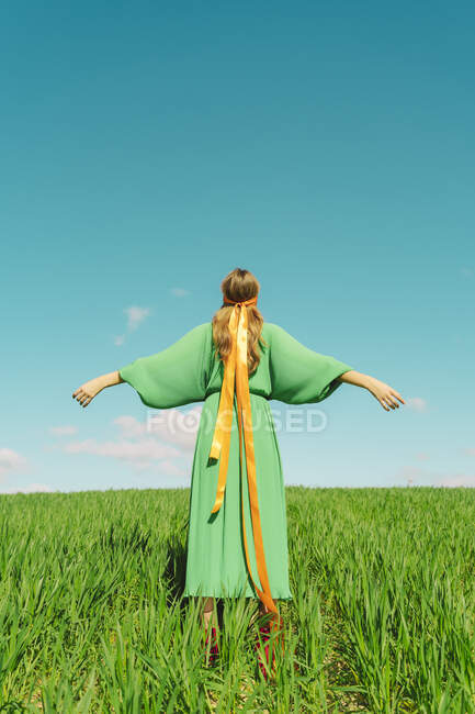 Rear view of young woman wearing a green dress standing in a field with a ribbon around her head — Stock Photo