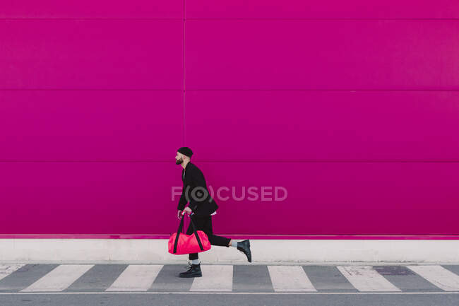 Young man with travelling bag running in front of a pink wall — Stock Photo