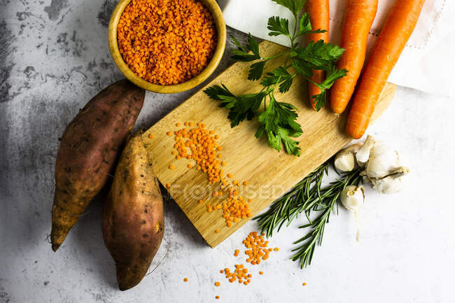 Studio shot of cutting board, bowl of red lentils, sweet potatoes, carrots, rosemary, parsley and garlic — Stock Photo