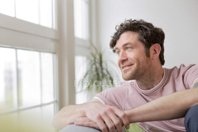 Sorrindo homem sentado no sofá em casa olhando para longe — Fotografia de Stock