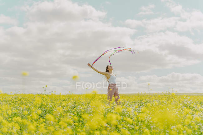 Giovane donna felice che si muove con nastri colorati in un prato fiorito in primavera — Foto stock