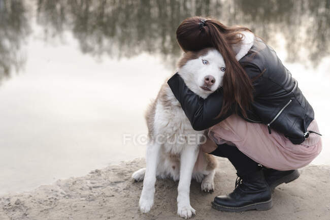 Mulher abraçando seu husky na borda da água — Fotografia de Stock