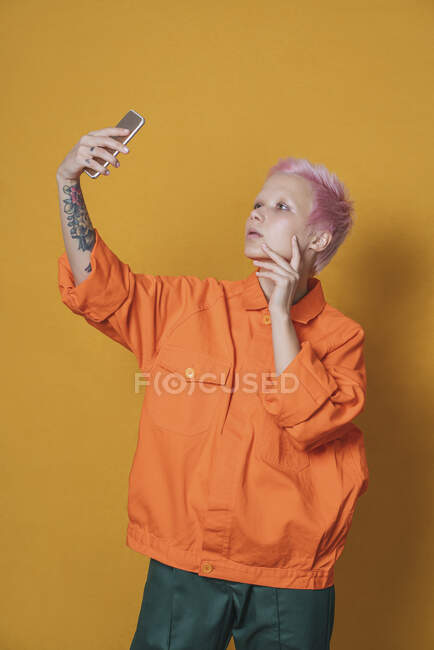 Портрет молодої жінки з рожевим волоссям, одягненої в помаранчеву куртку, селфі з смартфоном. — стокове фото