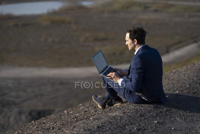 Maduro hombre de negocios utilizando el ordenador portátil en una punta de mina en desuso - foto de stock