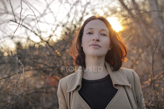 Чудова зріла жінка стоїть проти мертвих рослин у лісі під час заходу сонця. — стокове фото