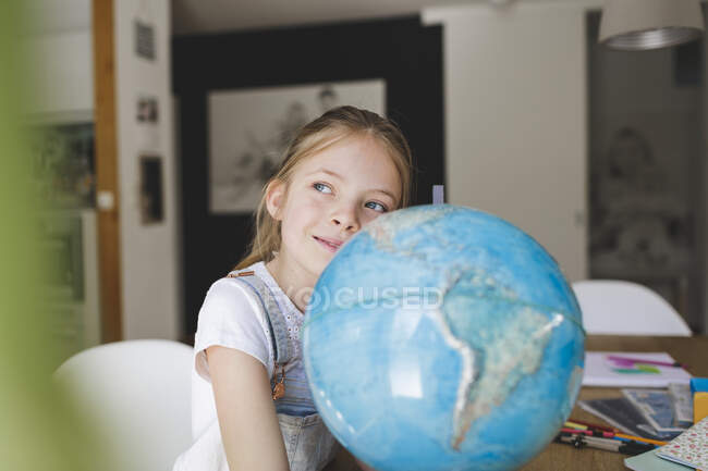 Portrait of confident girl with globe at home looking at distance — Stock Photo