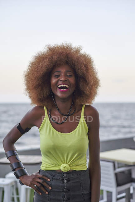 Portrait of laughing woman with afro hairstyle standing in front of the sea — Stock Photo
