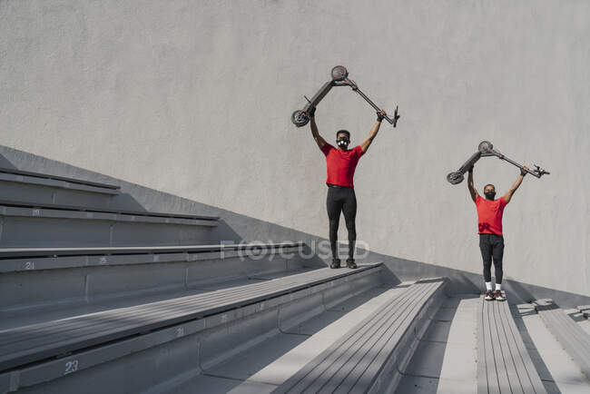 Sportsmen wearing face masks lifting up scooters on stairs — Stock Photo