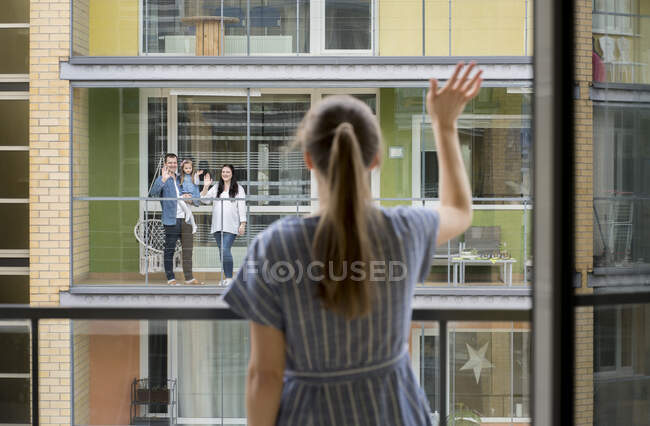 Vue arrière de la femme debout sur le balcon saluant ses voisins — Photo de stock