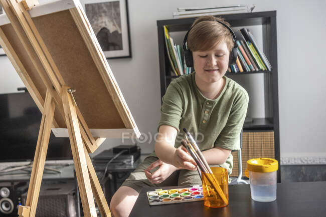 Boy painting at easel and listening to music — Stock Photo