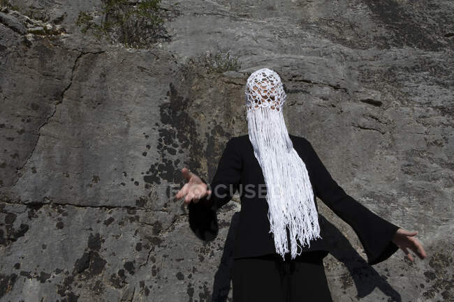 Mujer con tocado blanco de ganchillo con flecos en frente de la cara de roca - foto de stock