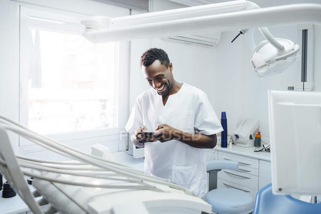 Buon dentista usando il cellulare nel suo studio medico — Foto stock