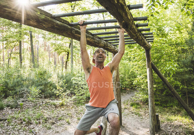 Счастливый человек, зависающий на обезьяньих барах во время занятий в парке — стоковое фото