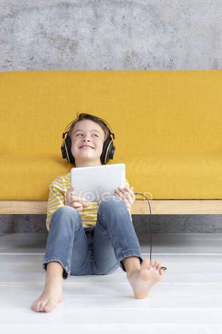Хлопчик грає з планшетом і в навушниках на жовтому дивані. — стокове фото