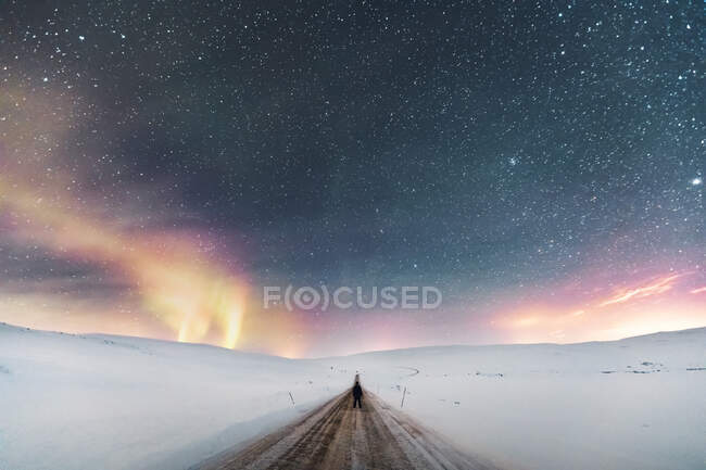 Man standing on country road under starry sky with northern lights, Lebesby, Noruega — Fotografia de Stock