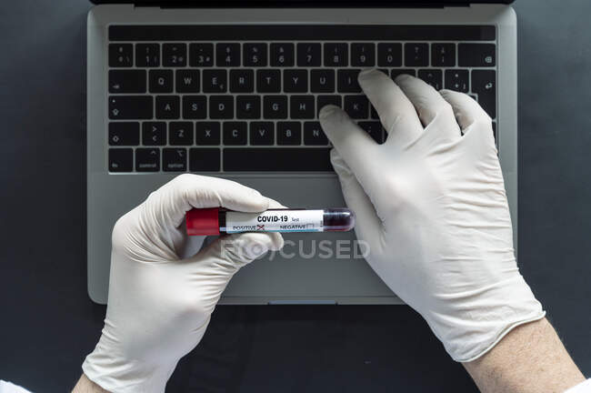 Лікар аналізує зразок COVID-19 під час друку на ноутбуці за столом у лабораторії. — стокове фото