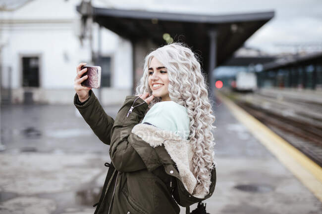 Portrait de jeune femme souriante prenant selfie avec smartphone sur la plate-forme — Photo de stock