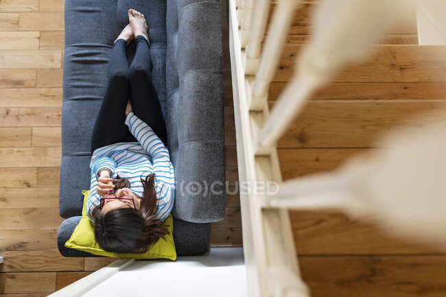 Mujer llamando y sentada en el sofá en casa, desde arriba - foto de stock