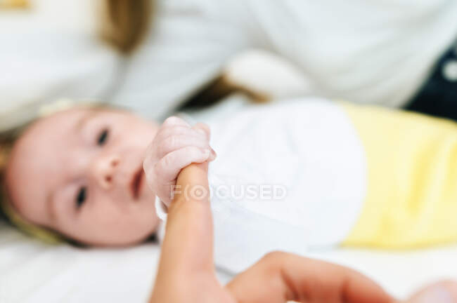 Дитина лежить на ліжку, тримаючи палець дорослої людини. — стокове фото