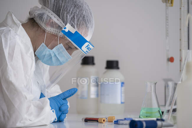 Женщина в защитной одежде сидит за столом и изучает образец крови. — стоковое фото